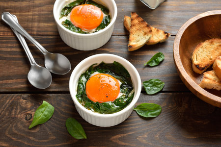 Eggs en cocotte (baked eggs) in ramekins with cream, cheese and spinach on wooden background. Close up viewの写真素材