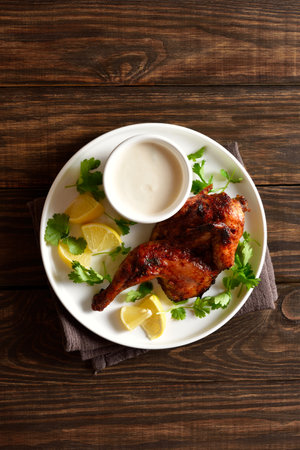 Roasted half chicken served with sauce on white plate over wooden background with free space. Tasty grilled chicken meat for dinner. Top view, flat layの写真素材