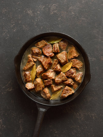 Braised beef in cast iron skillet over dark stone background. Beef goulash with gravy. Top view, flat layの写真素材