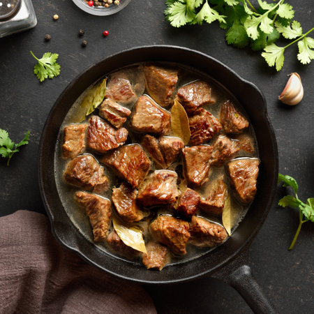 Braised beef in cast iron skillet over dark stone background. Beef goulash with gravy. Top view, flat layの写真素材