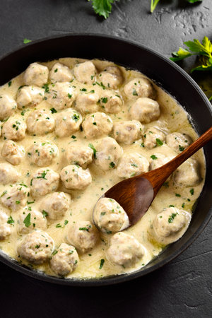 Delicious homemade Swedish meatballs with creamy white sauce in pan on black stone background. Close up viewの写真素材