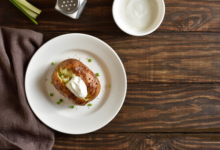 Baked potato with sour cream and green onion on plate over wooden background with free space. Top view, flat layの写真素材