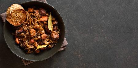 Close up view of traditional polish Bigos in bowl over dark stone background with copy space. Stewed cabbage with sauerkraut, mushrooms, smoked meats and spices. Top view, flat layの写真素材