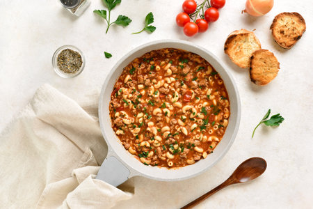 One pot meal with ground beef, pasta and vegetables simmered in tomato sauce in cooking pan on light stone background. Top view, flat layの写真素材