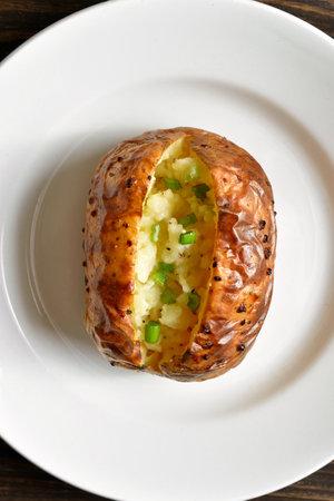 Close up view of oven baked potato with green onion on white plate. Top view, flat layの写真素材