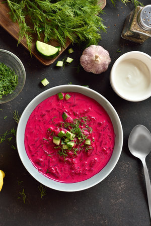 Cold summer soup. Beet cream soup with yogurt, cucumbers and dill in bowl on dark background. Top view, flat layの写真素材