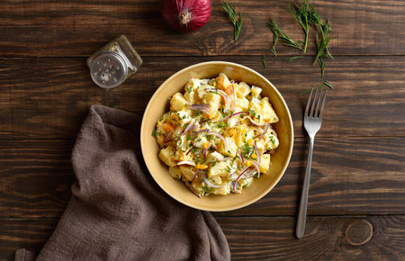 Warm potato salad with egg, pickle, red onion with mayonnaise and yogurt dressing in bowl on wooden background. Top view, flat layの写真素材