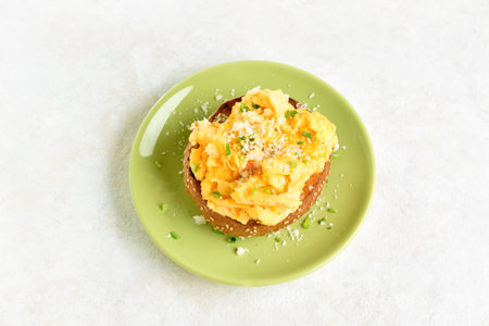 Diet scrambled eggs on toasted brioche bun on green plate on light background. Tasty meal for...
