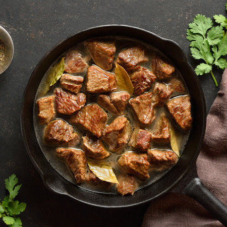 Braised beef in cast iron skillet on dark stone background. Beef goulash with gravy. Top view, flat layの写真素材