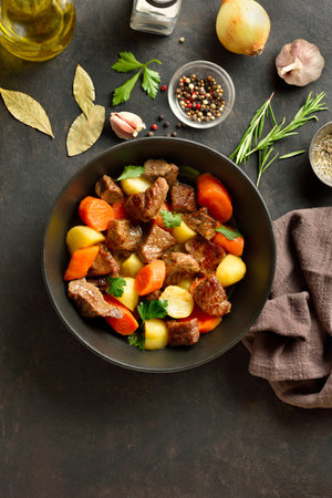 Beef stew with potatoes, carrots and greens in bowl over dark stone background. Comfort healthy food for dinner. Top view, flat layの写真素材