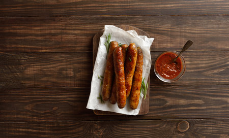 Roasted juicy sausages served with tomato sauce on wooden background. Country style. Top view, flat layの写真素材