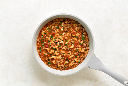 One pot meal with ground beef, pasta and vegetables simmered in tomato sauce in cooking pan on light stone background. Top view, flat layの写真素材