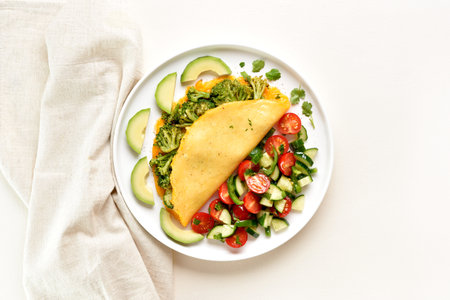 Omelet with roasted broccoli and cheese served with salad from fresh vegetables on white plate on light background. Healthy diet food concept. Top view, flat layの写真素材
