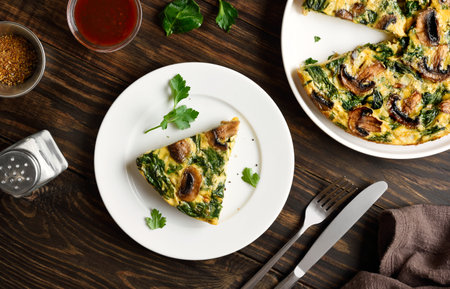 Frittata with spinach and champignon mushrooms on white plate on brown wooden table. Top view, flat layの写真素材