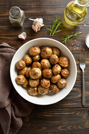 Roasted baby potatoes with olive oil, garlic and herbs in white bowl on brown wooden background. Top view, flat layの写真素材