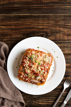 Lasagna with ground beef, ricotta cheese and tomato sauce on white plate on wooden background with free space. Top view, flat layの写真素材