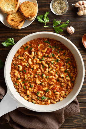 Macaroni with ground beef with vegetables in tomato sauce in skillet on wooden table. Top view, flat layの写真素材