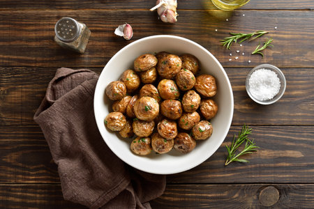Oven baked baby potatoes with olive oil, garlic and herbs in white bowl on wooden table. Top view, flat layの写真素材