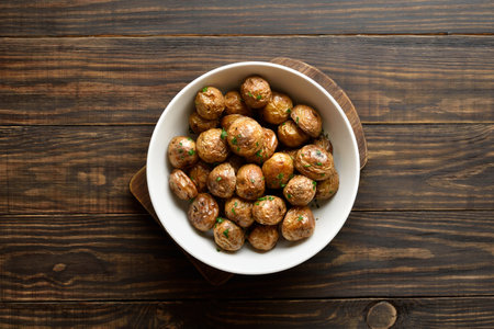 Roasted baby potatoes with olive oil, garlic and herbs in white bowl on brown wooden background. Top view, flat layの写真素材