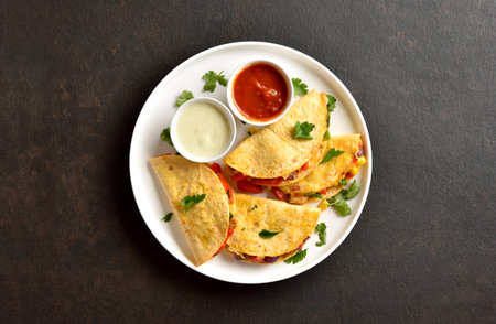 Homemade quesadilla with fresh vegetables served with sauce on white plate on brown stone background. Top view, flat layの写真素材