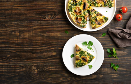 Frittata with spinach and champignon mushrooms on white plate on brown wooden background with free space. Top view, flat layの写真素材
