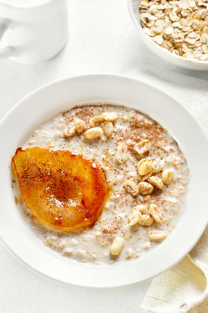 Oat porridge with caramelized pear and peanut in bowl over white background. Close up viewの写真素材