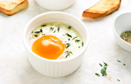 Eggs en cocotte (baked eggs) in ramekin on light stone background. Close up viewの写真素材