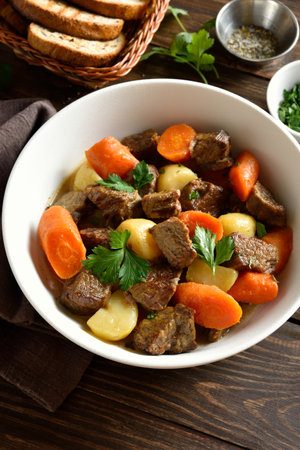 Beef meat stewed with potatoes, carrots and spices in white bowl on wooden table. Comfort healthy food for dinner. Close up viewの写真素材