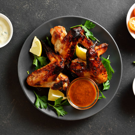 Barbecue chicken wings served with sauce on dark stone background. Tasty grilled chicken meat for dinner. Top view, flat layの写真素材