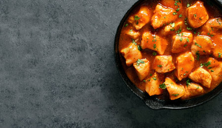 Close up view of sweet and spicy sliced chicken breast with sauce in cast iron pan on dark stone background with copy space. Top view, flat layの写真素材