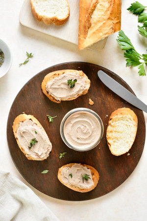 Chicken liver pate on toasted bread on wooden cutting board on light background. Top view, flat layの写真素材