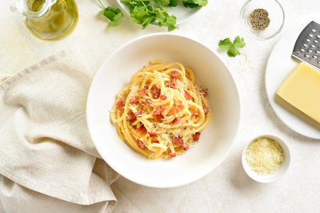 Italian pasta dish with crisp pancetta, parmesan cheese and black pepper in white ceramic bowl over light stone background. Top view, flat layの写真素材