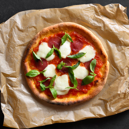 Pizza with mozzarella, pepperoni, tomato sauce and basil on parchment. Top view, flat lay.の写真素材