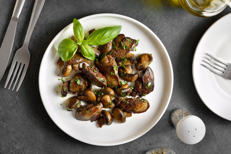 Fried chicken liver with mushrooms on white plate over dark stone background. Top view, flat layの写真素材