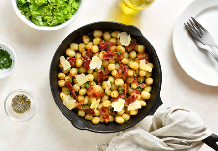 Potato gnocchi with bacon and parmesan cheese in cast iron pan over light background. Top view, flat layの写真素材
