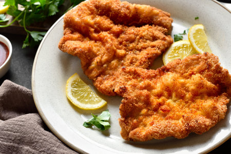 Close up view of schnitzel garnished with lemon slices and parsley leaves on white plate.の写真素材
