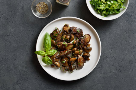 Fried chicken liver with mushrooms on white plate over dark stone background. Top view, flat layの写真素材