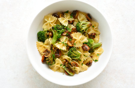 Close up view of farfalle pasta with roasted broccoli and mushrooms in white bowl on light background. Top view, flat layの写真素材