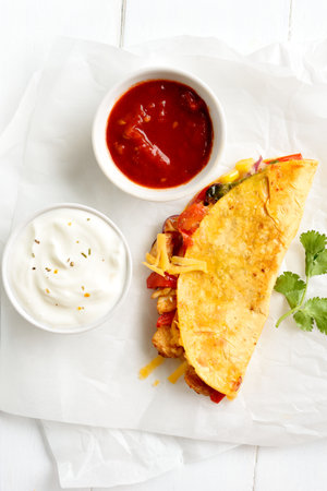Homemade quesadilla with roasted chicken breast, vegetables and cheese on parchment on white wooden background. Top view, flat layの写真素材