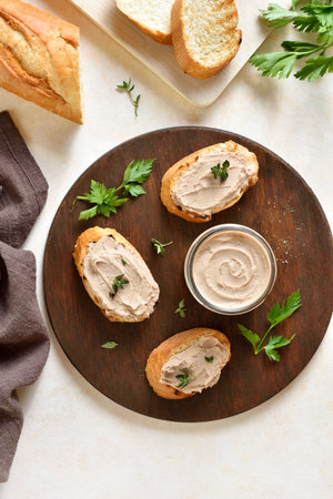 Chicken liver pate on toasted bread on wooden cutting board over light background. Top view, flat...