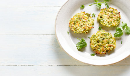 Close up view of zucchini fritters. Vegetable vegetarian zucchini pancakes on plate over white...