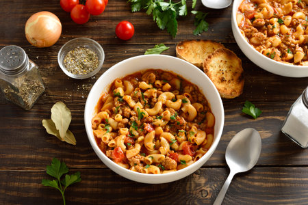 American goulash, dish with ground beef and elbow macaroni in tomato sauce in bowl on wooden table. Close up viewの写真素材