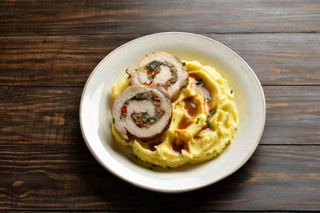 Slices of pork roll with mushrooms, cheese, sun dried tomatoes in gravy sauce served with mashed potatoes on light plate on brown wooden background. Close up viewの写真素材