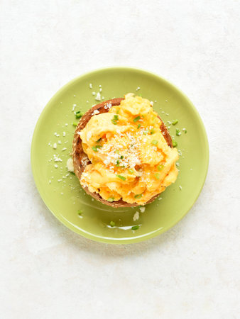 Diet scrambled eggs on toasted brioche bun on green plate on light background. Tasty meal for breakfast or brunch. Top view, flat layの写真素材