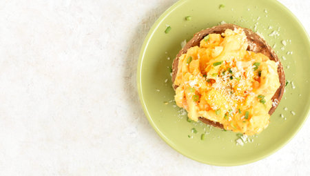 Close up view of diet scrambled eggs on toasted brioche bun on green plate on light background with...