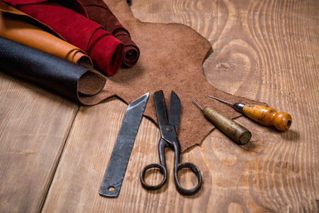 Set of leather craft tools on wooden background. Workplace for shoemaker. Piece of hide and working handmade tools on a work table.の写真素材