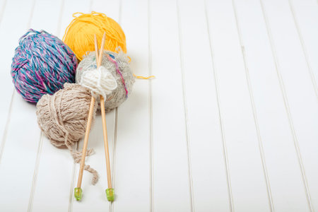 Knitting yarn balls and needles on the white wooden background.