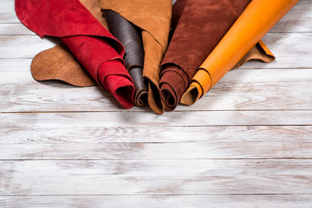 Brightly colored leather in rolls on the white wooden background. Leather craft. Copy space.