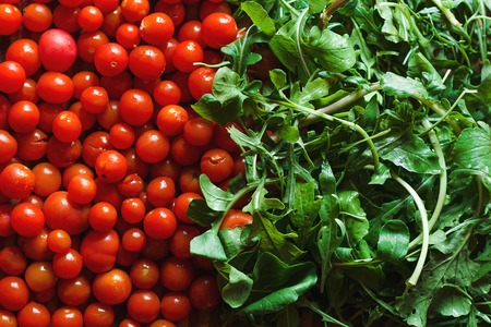 A lot of red fresh cherry tomatoes and arugula leaves close up. Top view.の写真素材