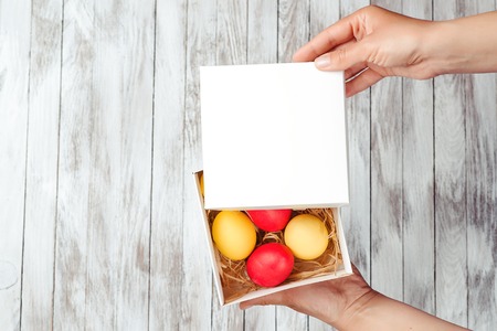 Female hands hold easter gift box with colorful eggs. Space for text.の写真素材